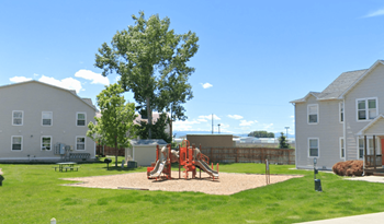 A playground with a slide and a tree in the middle of a grassy area.